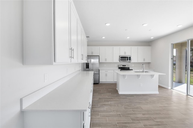 kitchen with sink, a breakfast bar area, appliances with stainless steel finishes, a kitchen island with sink, and white cabinets