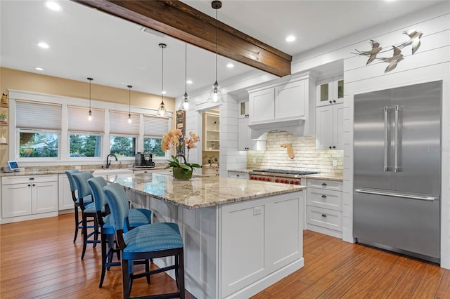 kitchen with a center island, built in fridge, white cabinets, light wood-type flooring, and beam ceiling