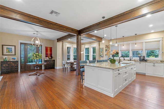 kitchen featuring white cabinets, a healthy amount of sunlight, a kitchen island with sink, and hanging light fixtures