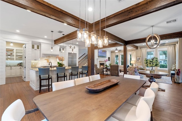 dining room featuring beam ceiling, sink, light hardwood / wood-style floors, and ceiling fan with notable chandelier