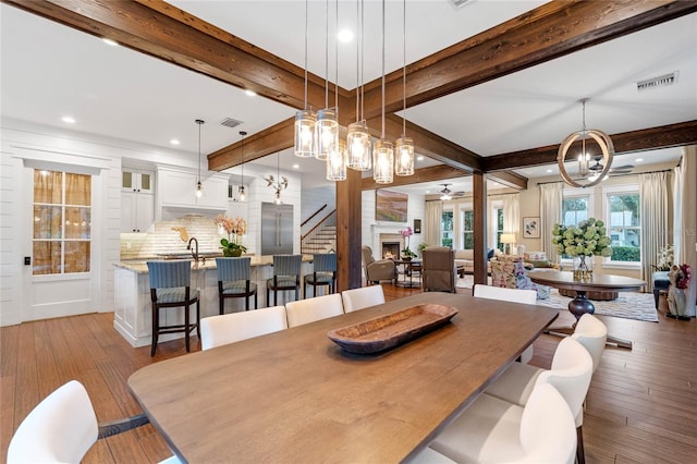 dining space featuring sink, beamed ceiling, ceiling fan with notable chandelier, and light wood-type flooring