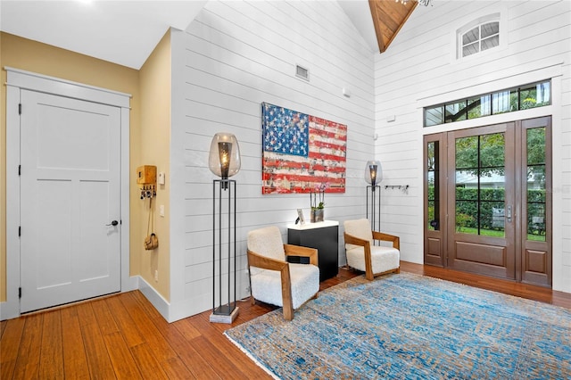 entrance foyer with wood-type flooring, high vaulted ceiling, and wooden walls