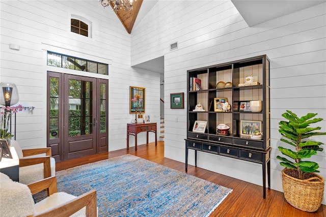 foyer featuring wooden walls, high vaulted ceiling, wood-type flooring, and a notable chandelier