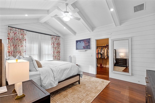 bedroom with wooden walls, wood-type flooring, a spacious closet, vaulted ceiling with beams, and a closet