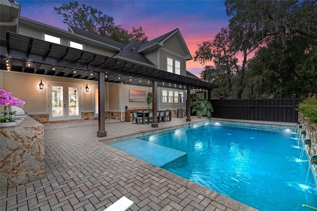 pool at dusk with pool water feature, a patio area, a pergola, and french doors