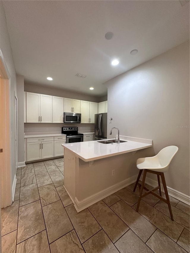 kitchen with a kitchen bar, sink, white cabinetry, appliances with stainless steel finishes, and kitchen peninsula