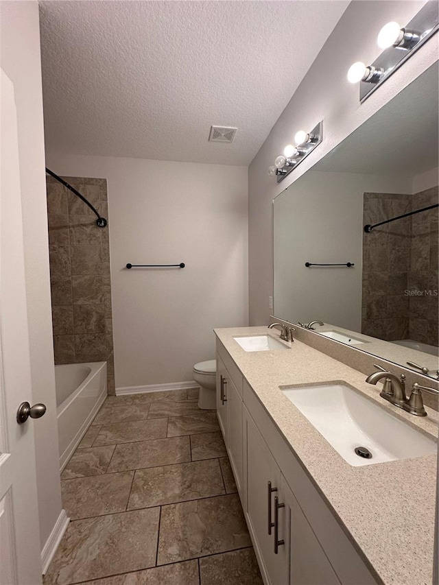 full bathroom with tiled shower / bath, vanity, toilet, and a textured ceiling