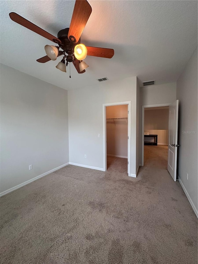 unfurnished bedroom with light carpet, a textured ceiling, a walk in closet, and ceiling fan