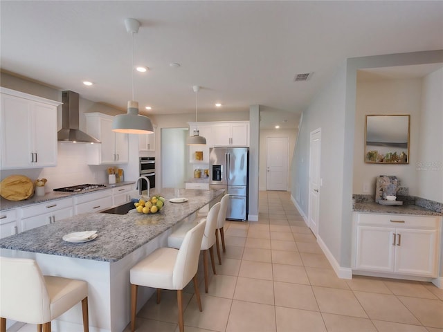 kitchen featuring stainless steel appliances, sink, wall chimney range hood, a center island with sink, and white cabinets