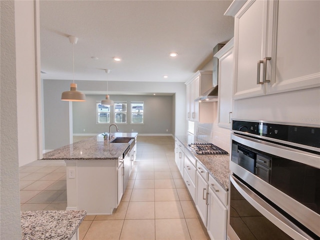 kitchen featuring hanging light fixtures, light stone counters, an island with sink, white cabinets, and appliances with stainless steel finishes