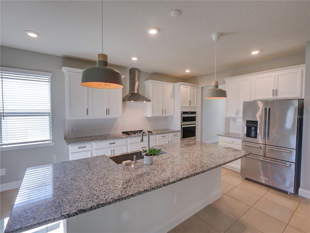 kitchen with wall chimney exhaust hood, stone counters, decorative light fixtures, and appliances with stainless steel finishes