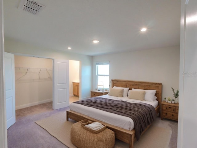 bedroom featuring light colored carpet, a spacious closet, and ensuite bath