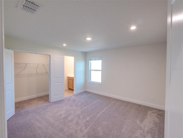 unfurnished bedroom with a walk in closet, a closet, and light colored carpet