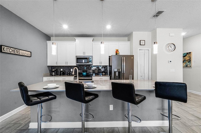 kitchen featuring a breakfast bar, stainless steel appliances, decorative light fixtures, white cabinets, and an island with sink