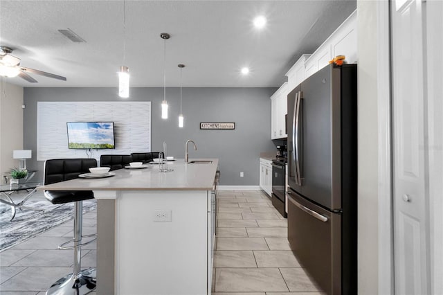 kitchen featuring a kitchen bar, stainless steel fridge, a kitchen island with sink, pendant lighting, and white cabinetry