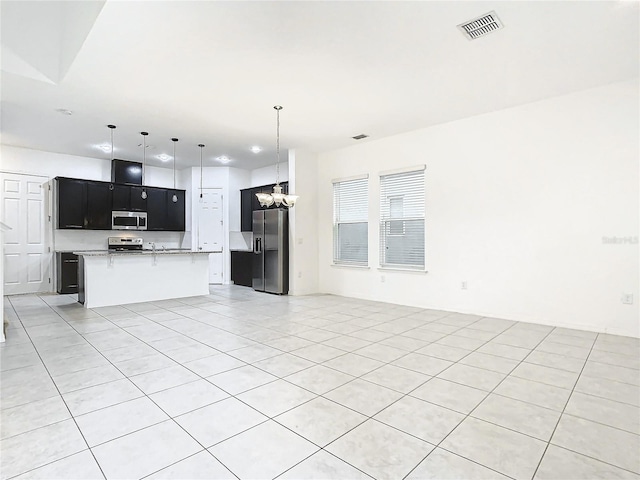 kitchen with a breakfast bar, an inviting chandelier, an island with sink, appliances with stainless steel finishes, and light tile patterned flooring