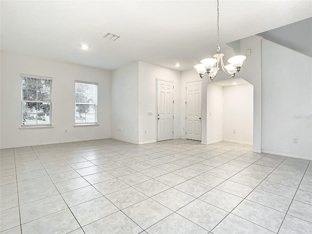 empty room with a notable chandelier and light tile patterned floors