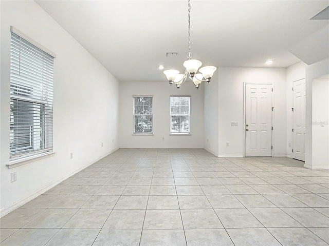 spare room featuring plenty of natural light, light tile patterned flooring, and a chandelier