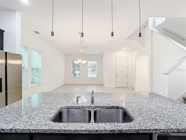 kitchen featuring light stone countertops, sink, an island with sink, and a notable chandelier