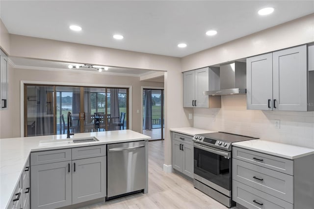 kitchen with gray cabinetry, wall chimney range hood, sink, and appliances with stainless steel finishes