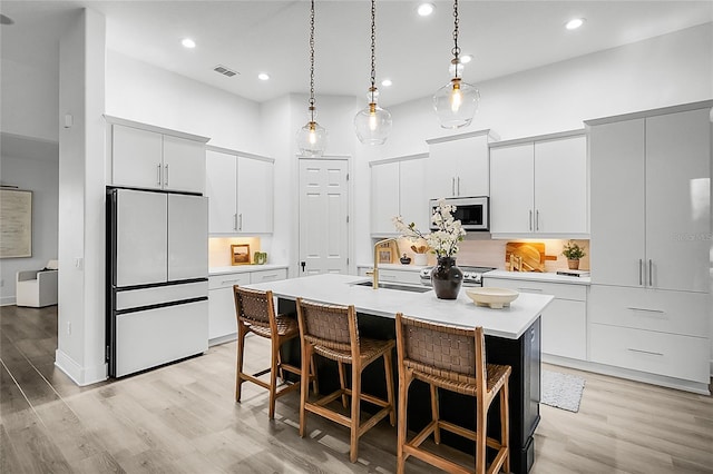 kitchen with sink, white fridge, light hardwood / wood-style floors, a kitchen island with sink, and white cabinets