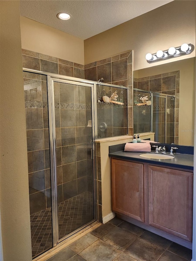 bathroom with vanity, a shower with shower door, and a textured ceiling