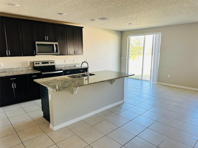 kitchen with light stone countertops, stainless steel appliances, a center island with sink, and sink