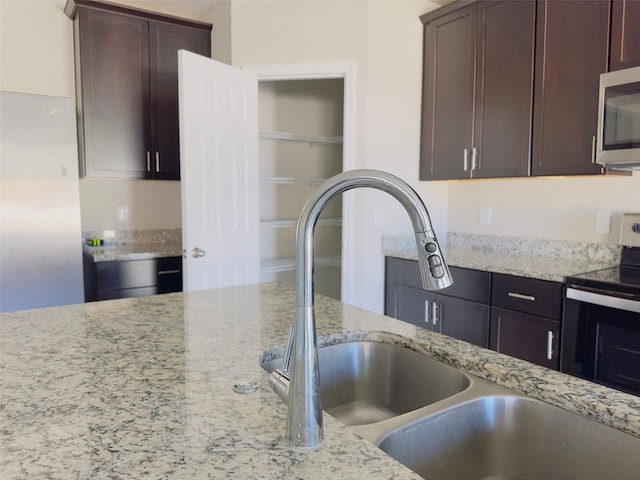 kitchen featuring dark brown cabinetry, light stone countertops, sink, and appliances with stainless steel finishes