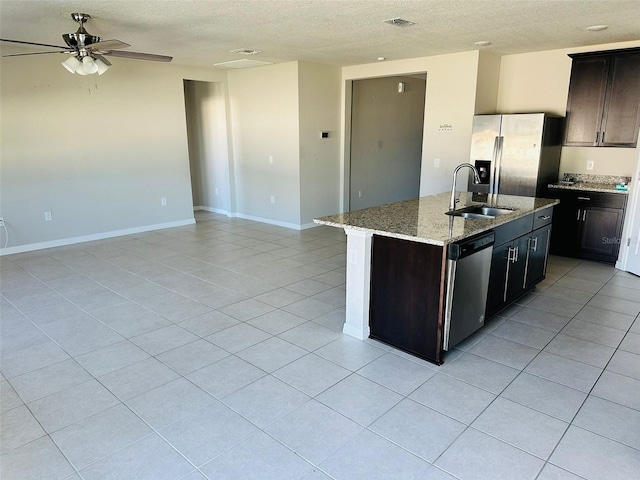 kitchen with sink, stainless steel appliances, light stone counters, a textured ceiling, and a center island with sink