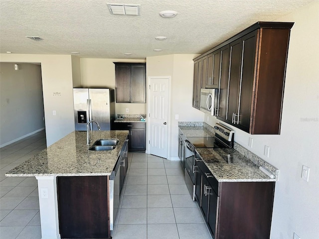 kitchen with appliances with stainless steel finishes, light stone counters, a kitchen island with sink, sink, and light tile patterned flooring