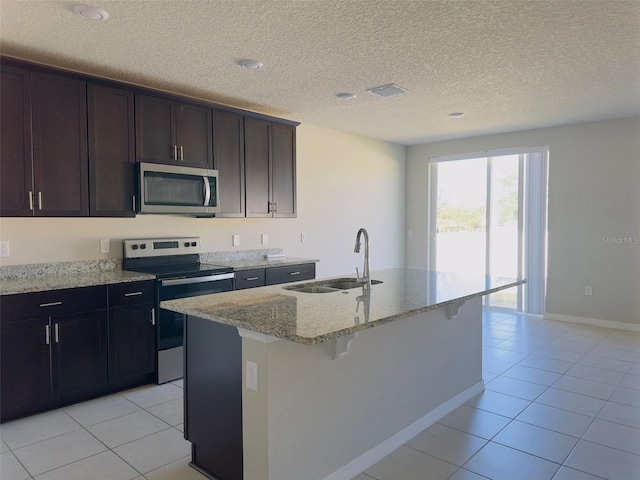 kitchen featuring light stone countertops, sink, a textured ceiling, a center island with sink, and appliances with stainless steel finishes