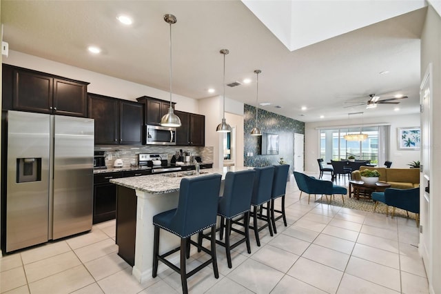 kitchen with ceiling fan, hanging light fixtures, a kitchen breakfast bar, a kitchen island with sink, and appliances with stainless steel finishes