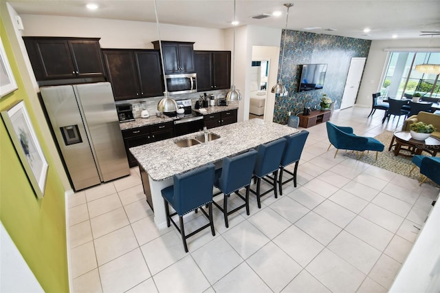 kitchen featuring a kitchen breakfast bar, light tile patterned floors, an island with sink, appliances with stainless steel finishes, and light stone counters