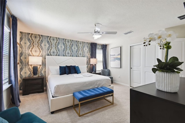 bedroom featuring ceiling fan, a closet, light carpet, and a textured ceiling