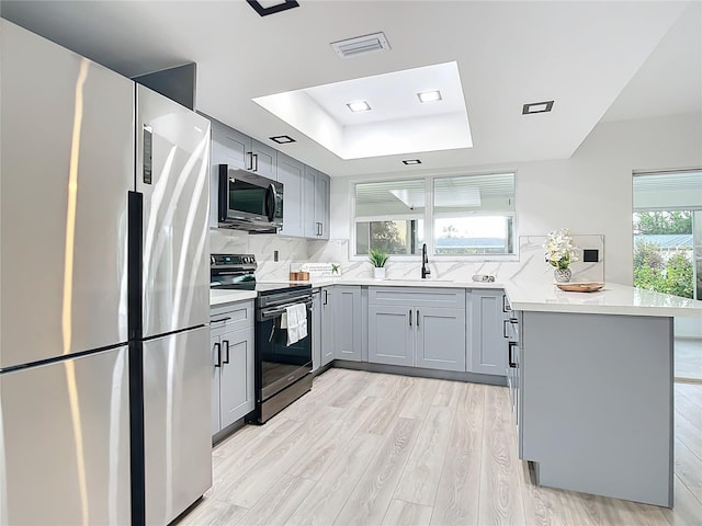 kitchen featuring a raised ceiling, sink, decorative backsplash, light wood-type flooring, and appliances with stainless steel finishes