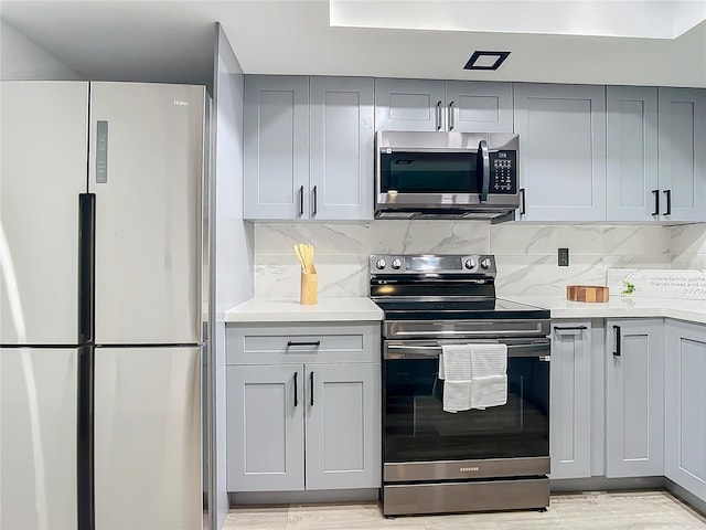 kitchen with decorative backsplash, gray cabinets, appliances with stainless steel finishes, and light hardwood / wood-style flooring