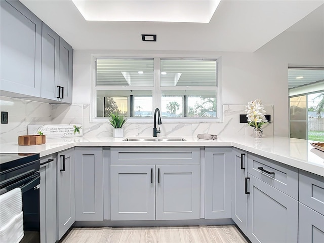 kitchen with decorative backsplash, light wood-type flooring, gray cabinets, and sink