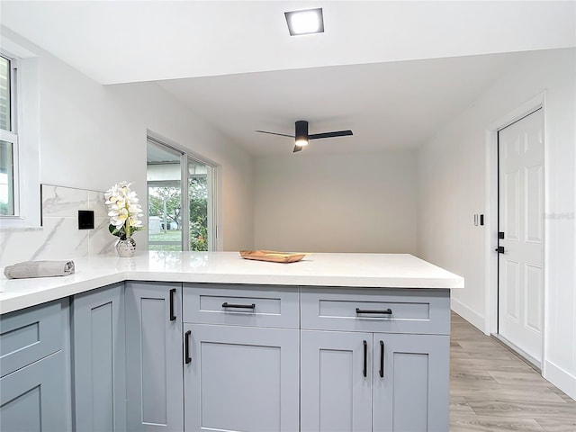 kitchen with gray cabinets, ceiling fan, light hardwood / wood-style floors, and backsplash