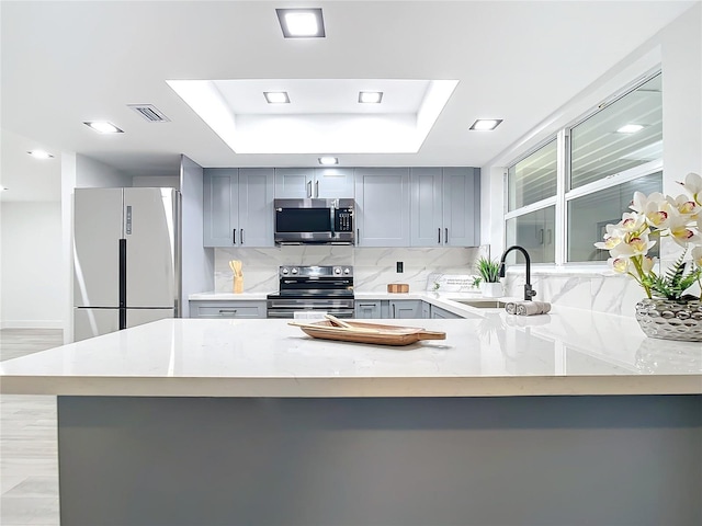 kitchen featuring kitchen peninsula, stainless steel appliances, light stone counters, and sink