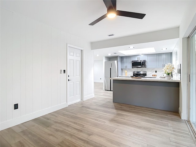 kitchen featuring light hardwood / wood-style flooring, ceiling fan, appliances with stainless steel finishes, tasteful backsplash, and kitchen peninsula