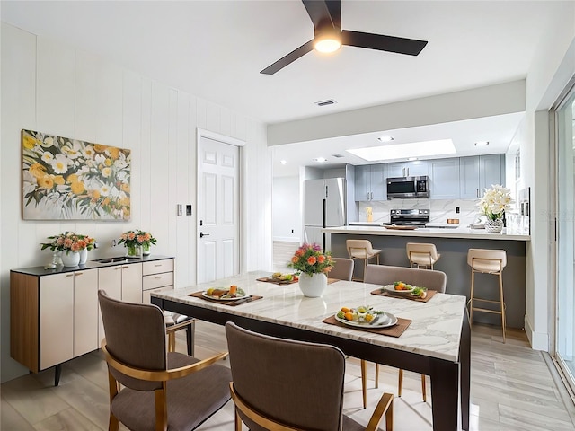 dining area with ceiling fan, wood walls, and light hardwood / wood-style flooring