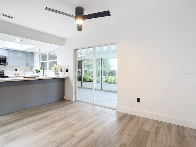 unfurnished living room with ceiling fan, sink, and light wood-type flooring