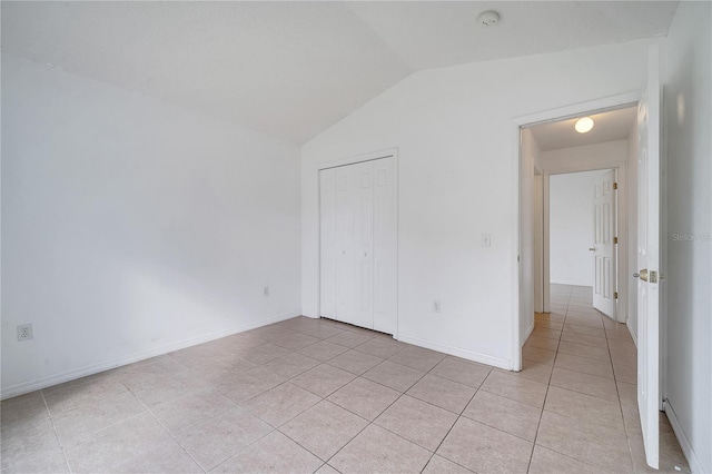 unfurnished bedroom with light tile patterned flooring, a closet, and vaulted ceiling