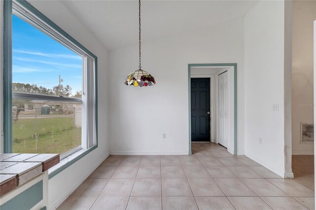 unfurnished dining area with light tile patterned floors, vaulted ceiling, and plenty of natural light