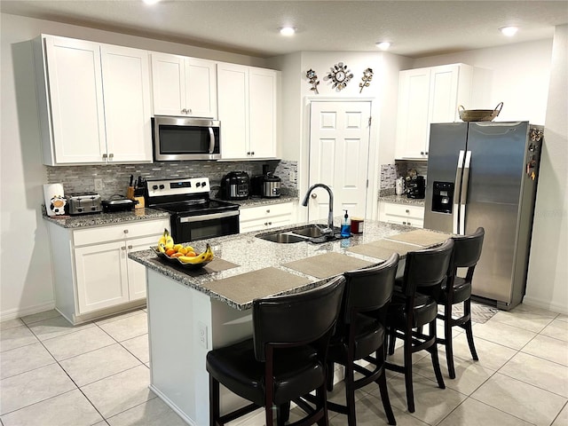 kitchen featuring a kitchen breakfast bar, white cabinets, an island with sink, and appliances with stainless steel finishes