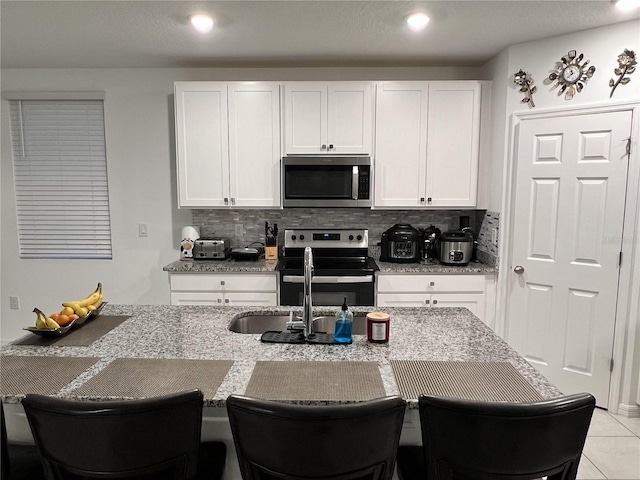 kitchen with a breakfast bar, light stone countertops, white cabinetry, and appliances with stainless steel finishes