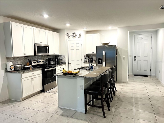 kitchen with a kitchen breakfast bar, stainless steel appliances, a kitchen island with sink, sink, and white cabinets