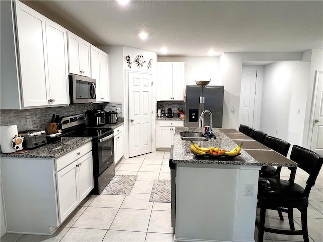 kitchen with sink, an island with sink, a kitchen bar, white cabinetry, and stainless steel appliances