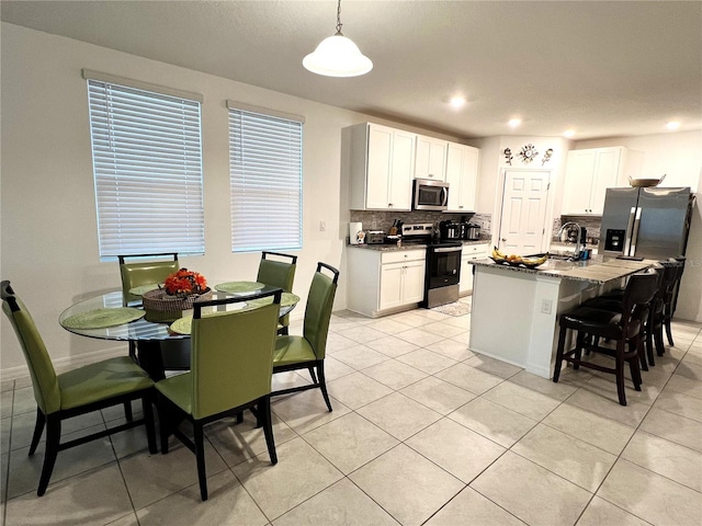 kitchen featuring dark stone countertops, an island with sink, decorative light fixtures, white cabinets, and appliances with stainless steel finishes