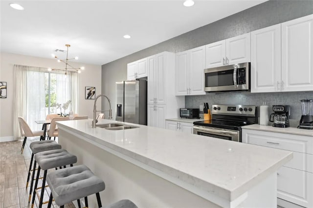 kitchen with sink, stainless steel appliances, light hardwood / wood-style flooring, a kitchen bar, and a kitchen island with sink